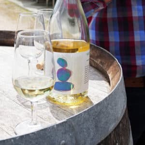 Étiquette du vin blanc Le Cairn sur bouteille, posée sur un fût de bois entre deux verres, création signée Julien Maurel, graphiste en Occitanie.